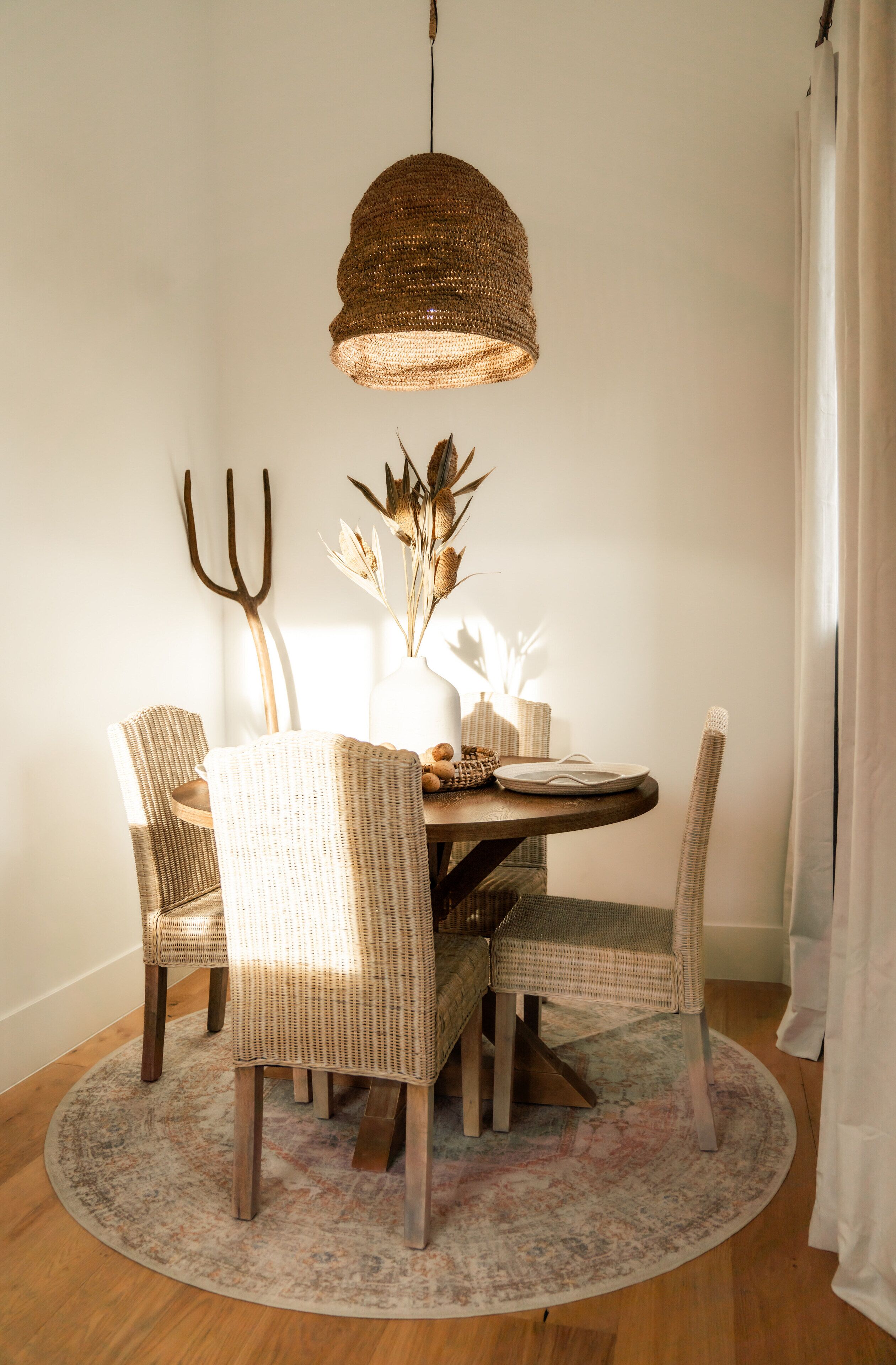 A dining area with wicker chairs, a round table, a woven pendant light, and a rustic rug.