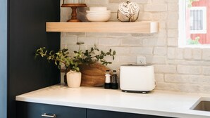 A kitchen with dark cabinets, white countertops, and a brick wall. There are wooden shelves with decorative items and a toaster on the counter. - The Silo Inn near Zion, Snow Canyon and Bryce Canyon! honeymoon getaway. 2023 (Washington)