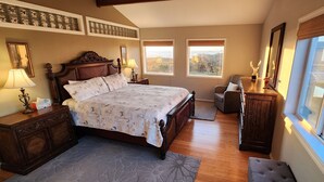 Een slaapkamer met een groot bed, twee nachtkastjes, een dressoir, een stoel en een raam met uitzicht.