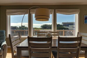 A dining area with a table and chairs, large windows with a view of a balcony and trees, and a hanging lamp.
