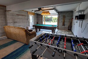 A room with a foosball table, a pool table, and a sofa.