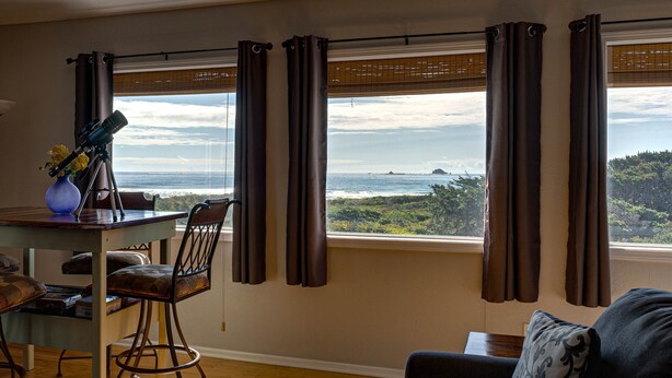Een kamer met uitzicht op de oceaan, een eettafel met stoelen en een bank.