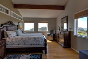 A bedroom with a large bed, a dresser, a chair, and a view of the outdoors through two windows.