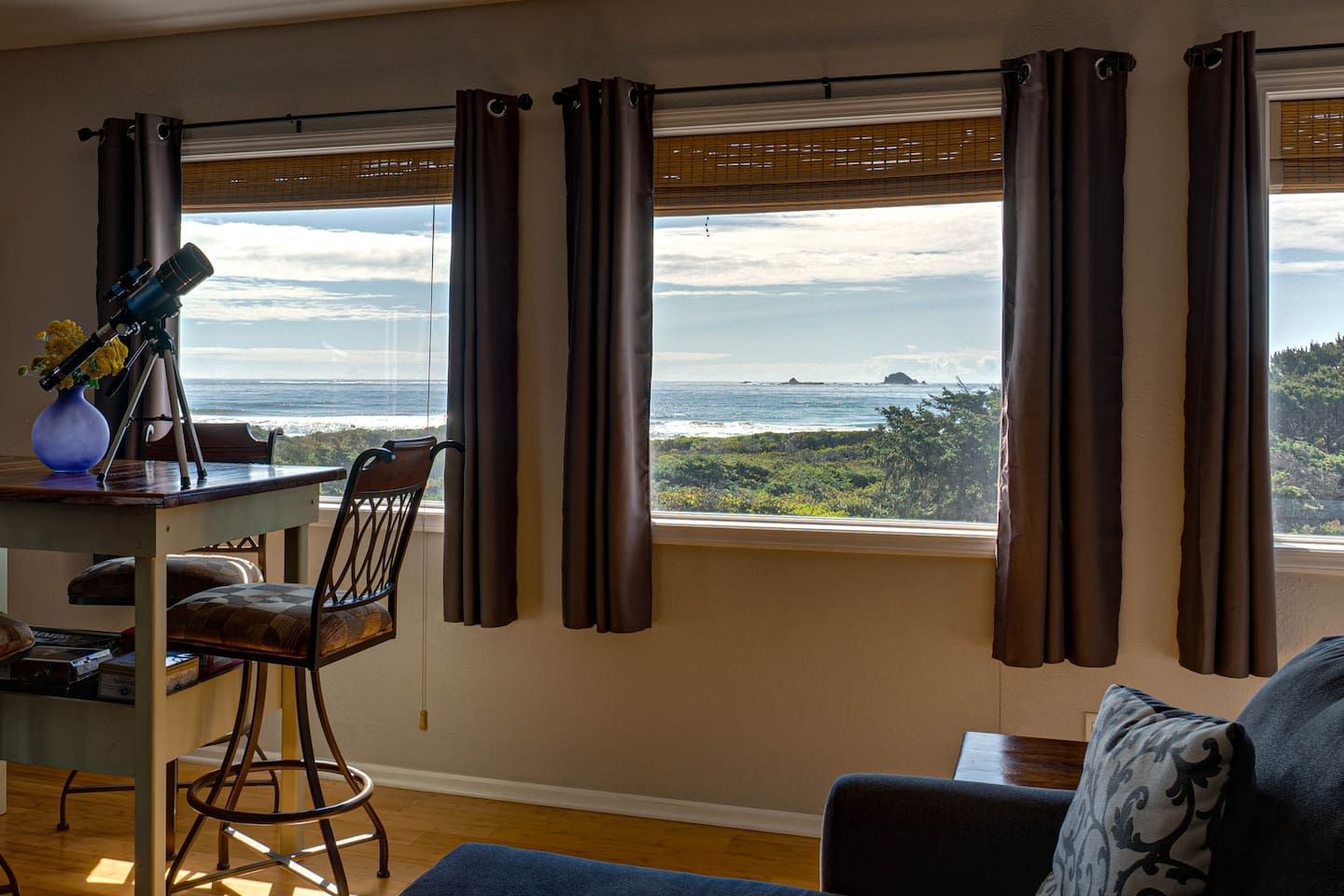 A room with a view of the ocean, a desk with a telescope, and a chair.