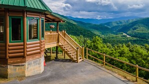 Eine Holzhütte mit einem grünen Dach, einer Holztreppe und Blick auf eine Berglandschaft.