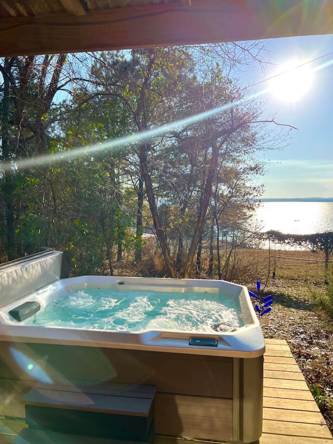 Jacuzzi con terraza de madera y vista a un lago y árboles.