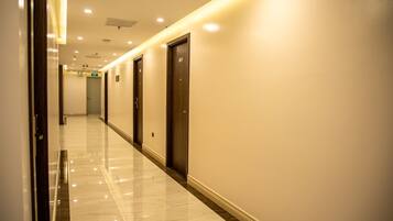 A hotel corridor with a polished marble floor, wooden doors, and recessed lighting.