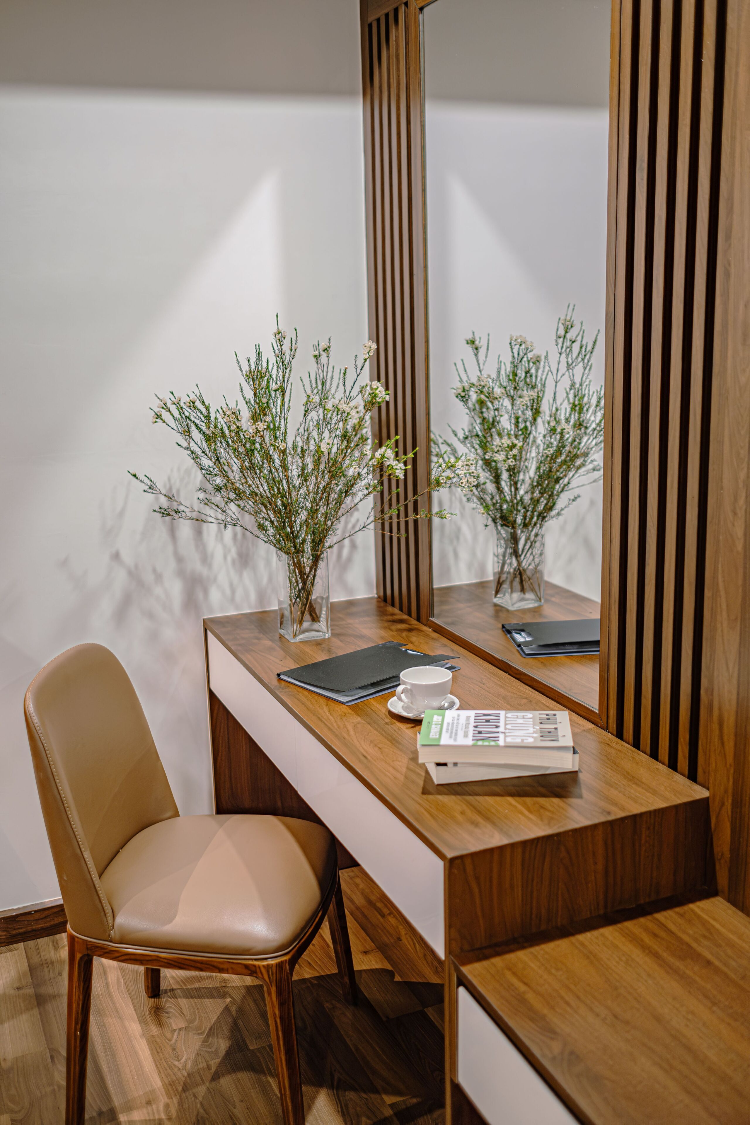 A wooden desk with a laptop, a cup, and a vase with plants.