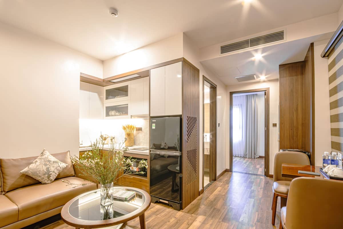 A modern hotel room with a sofa, a dining table, a kitchen area, and a separate dining area.