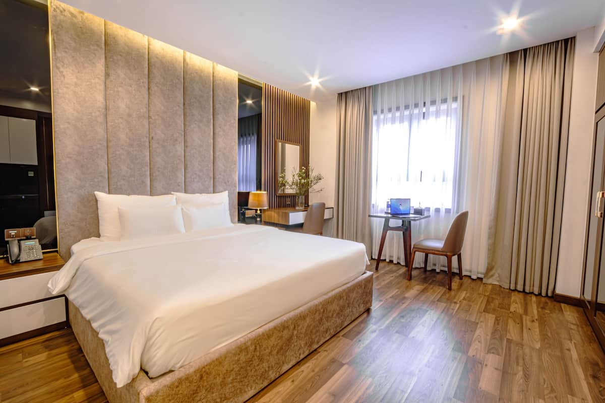 A hotel room with a large bed, a desk, a chair, and a mirror.