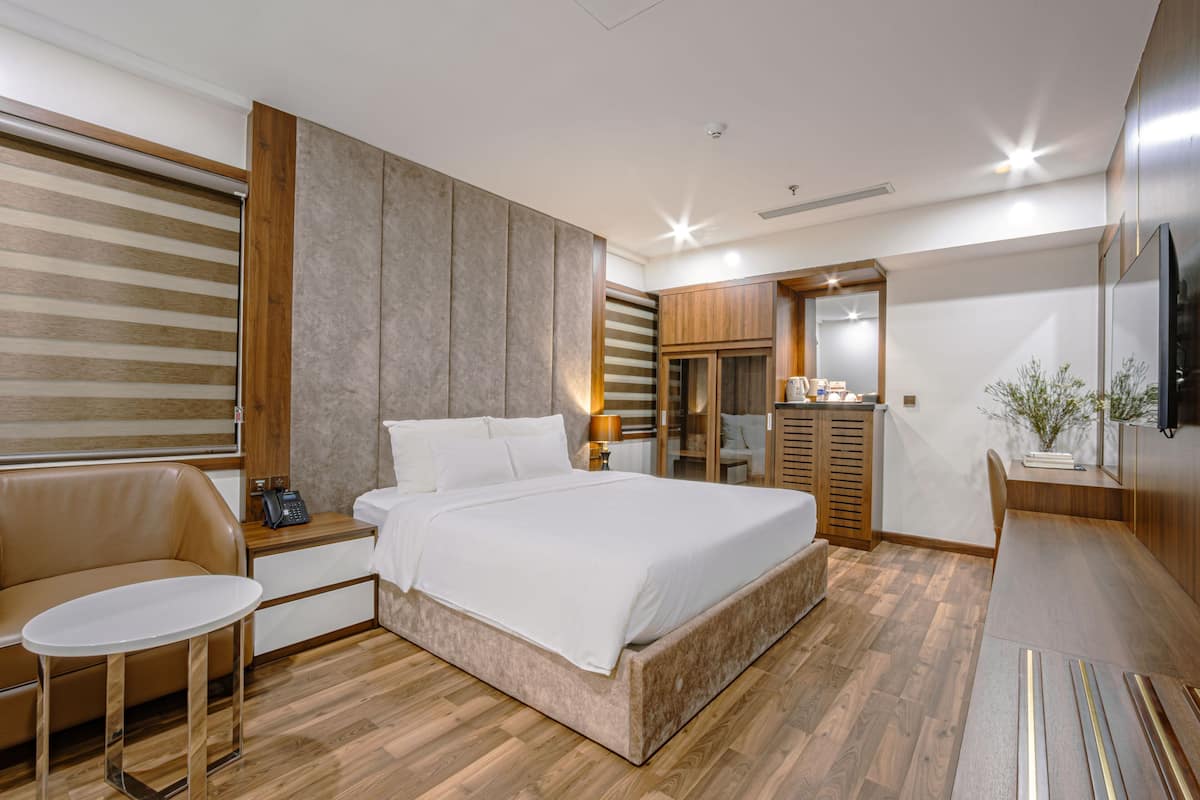 A modern hotel room with a large bed, a sofa, a small table, a desk, and a TV.