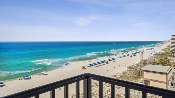 A beach view from a balcony with a clear sky, a sandy beach, and a few umbrellas. - Breathtaking views! 1 BR Gulf front condo w/2 pools on relaxing east side of PCB (Panama City Beach)