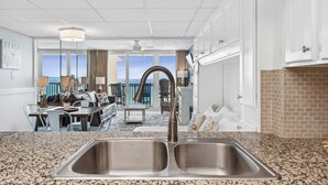 A kitchen with granite countertops, a double sink, and a view of the ocean through large windows. - Breathtaking views! 1 BR Gulf front condo w/2 pools on relaxing east side of PCB (Panama City Beach)