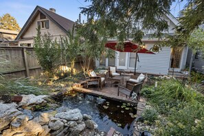 A backyard with a pond, patio furniture, and a house.