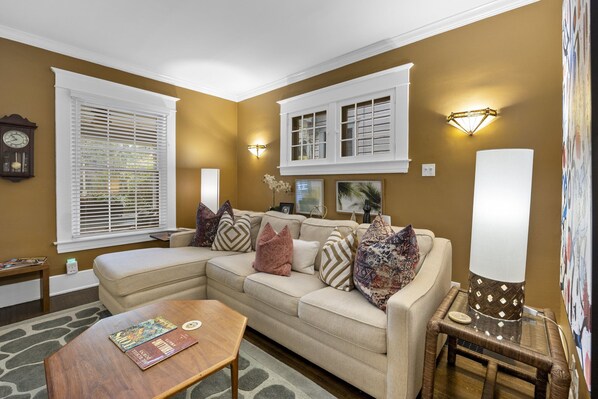 A living room with a beige sectional sofa, a coffee table, a clock on the wall, and a lamp on a side table.