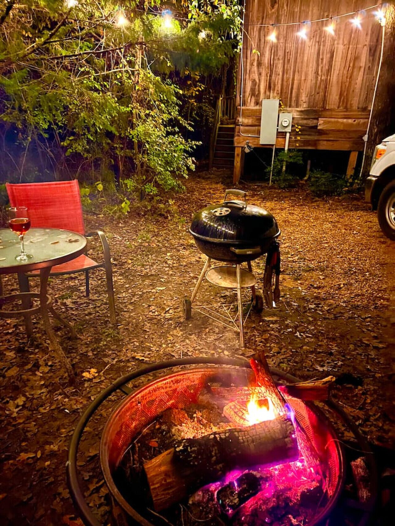 A backyard with a fire pit, a grill, and a table with a red chair.