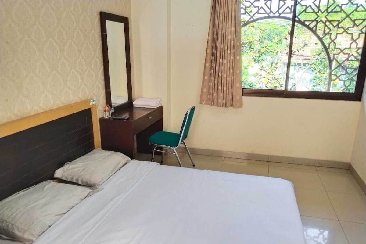 Une chambre d’hôtel équipée d’un lit, d’un bureau, d’une chaise, d’un miroir et d’une fenêtre donnant sur un paysage verdoyant.