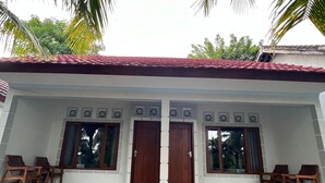 Un edificio con techo de tejas rojas, dos puertas de madera y un porche cubierto con sillas de madera.