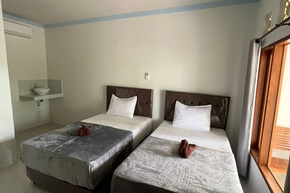 A room with two beds, a small sink, and a window.