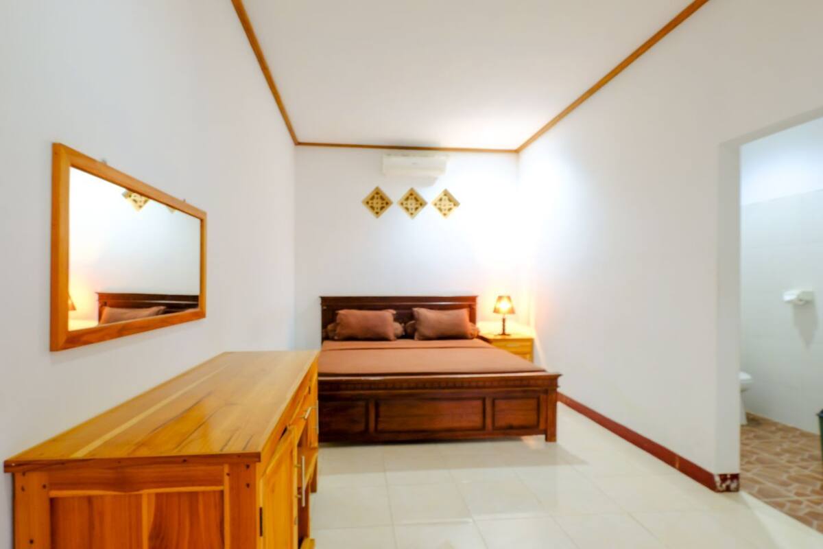 A bedroom with a wooden bed, a wooden dresser, a mirror, and a bedside lamp.