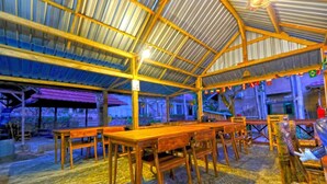 Espacio interior con techo alto y vigas de madera, con mesas y bancos dispuestos para sentarse.