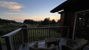 A wooden deck with wicker furniture, overlooking a grassy area with trees and a small building. - The ocean meets the meadow at the forest's edge. Private beach. Soak under stars (Manchester)