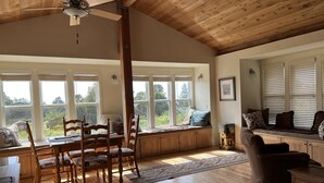 A spacious room with a dining area, a seating area with a sofa and armchairs, large windows with blinds, and a ceiling fan. - The ocean meets the meadow at the forest's edge. Private beach. Soak under stars (Manchester)