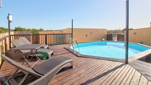 En træterrasse med pool, liggestole og et træhegn.
