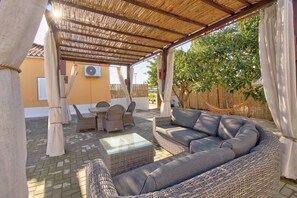 Un espace extérieur abrité, aménagé avec des meubles en osier, une table et un hamac.