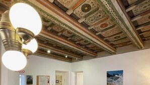 Habitació amb sostre de fusta, un sofà vermell, una taula de menjador amb posa taules i una catifes amb dibuixos.