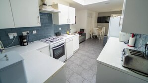 A compact kitchen with a gas stove, oven, and a small dining area with a table and chairs. - Stunning studio next to restaurants! (Birmingham)