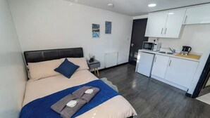 A modern hotel room with a bed, a small bedside table, a microwave, and a kitchenette area. - Modern Studio next to University of Birmingham (Birmingham)