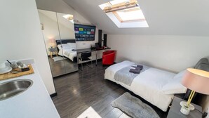 Habitación de hotel compacta con kitchenette, una cama, un escritorio y un televisor montado en la pared.