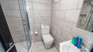 A modern bathroom with a glass shower enclosure, a toilet, and a sink with toiletries.