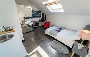 A modern, compact room with a skylight, a bed, a desk, and a kitchenette.