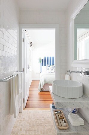Un baño con lavamanos blanco, espejo y toallero.