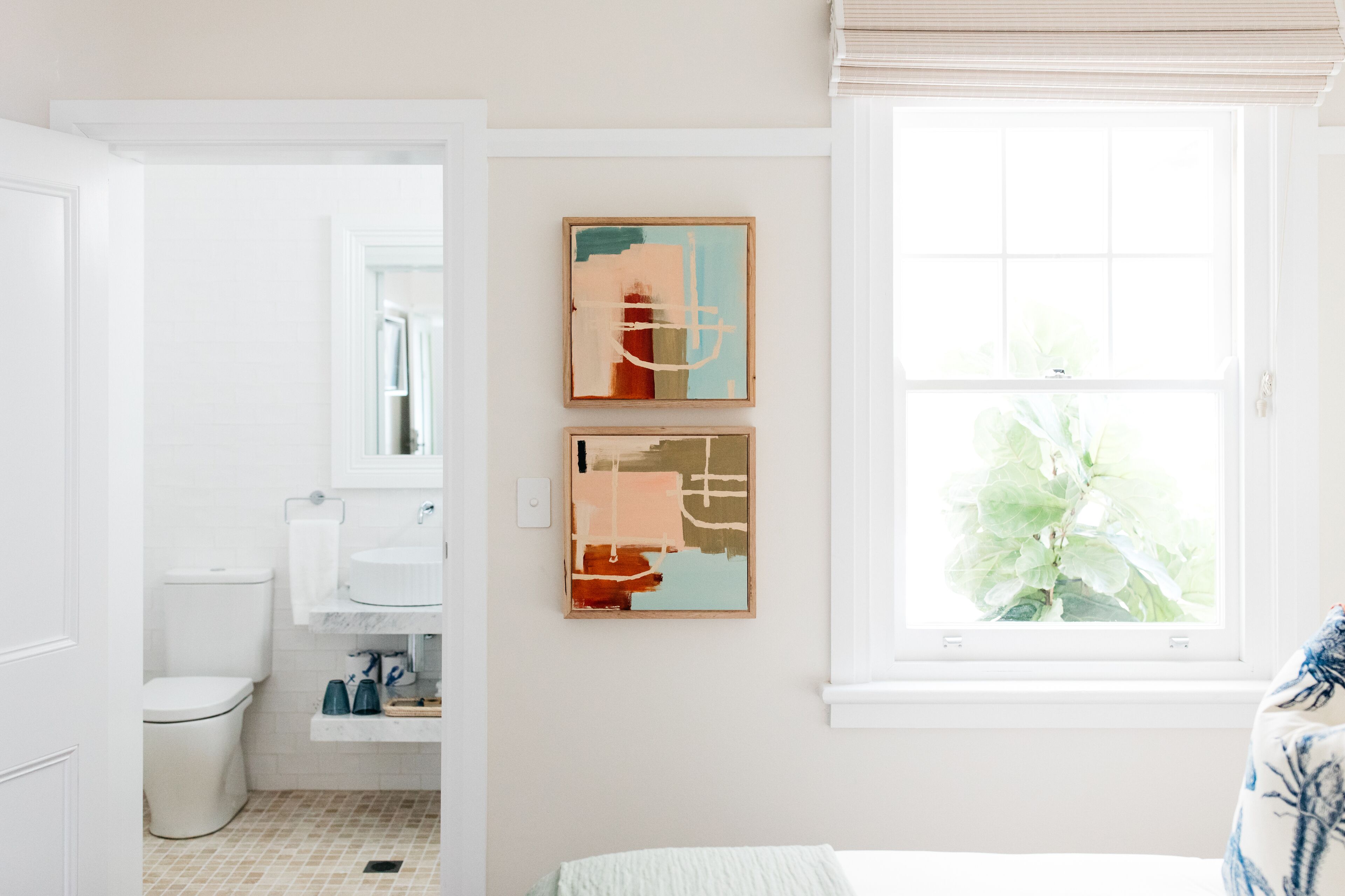 A modern bathroom with a toilet, sink, and shower. There are two abstract paintings on the wall.