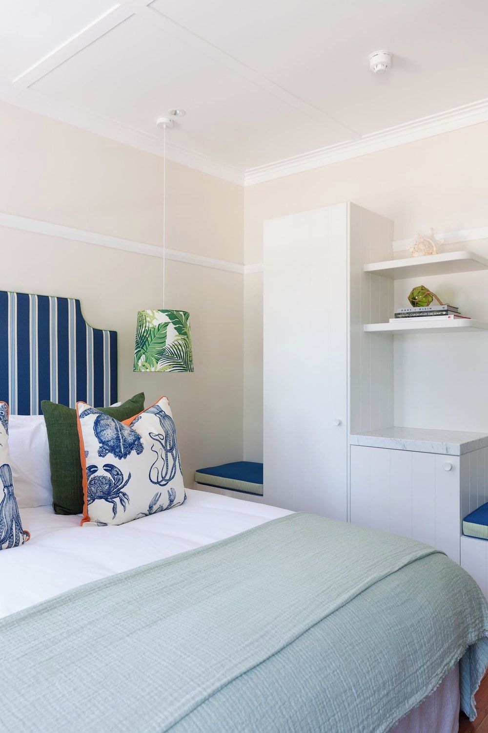 A bedroom with a bed, a wardrobe, a shelf with books, and a hanging plant.