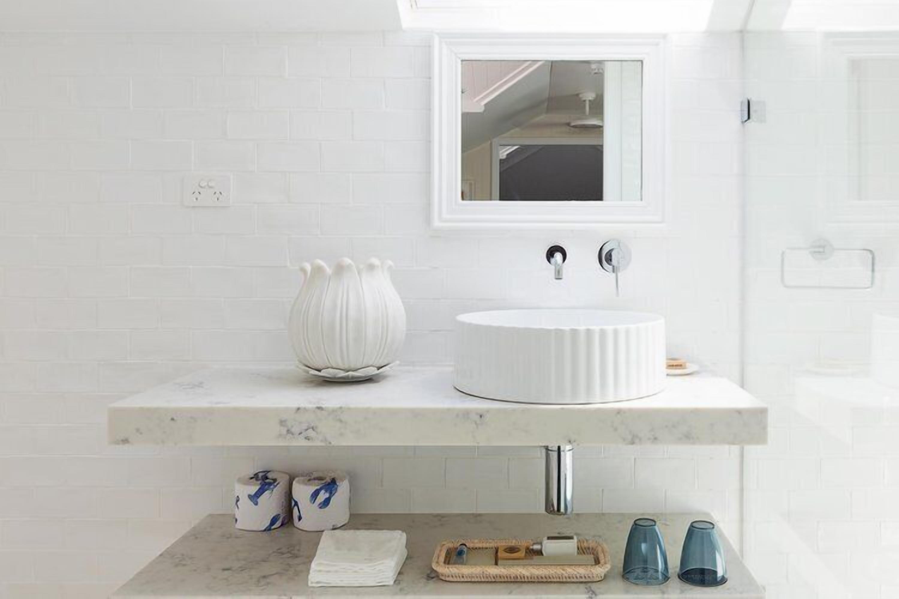 A bathroom with a white sink, a mirror, and a marble countertop. There are two rolls of toilet paper and a towel on the counter.