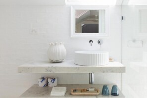 Un baño con un lavamanos blanco, un espejo y una encimera de mármol. Hay dos rollos de papel higiénico y una toalla en la encimera.