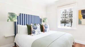 A bedroom with a striped headboard, a large window with a view of trees, and a bed with multiple pillows. - Barrenjoey House  (Palm Beach)