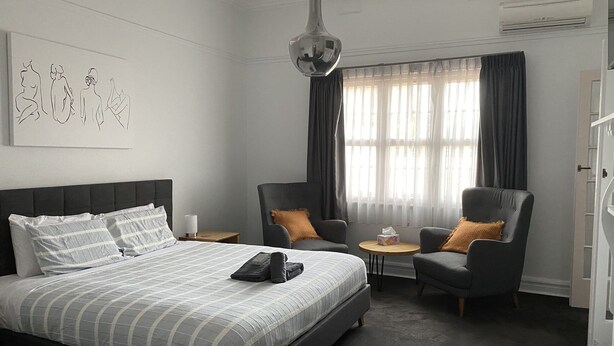 A modern hotel room with a large bed, two armchairs, a small table, and a large window with curtains. - Avon Homestay (Northam)