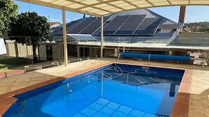 A swimming pool with a clear blue water surface, surrounded by a covered patio area with a roof. - Avon Homestay (Northam)