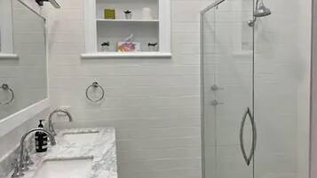 Une salle de bain avec un meuble-lavabo blanc, une cabine de douche en verre et un carrelage décoratif.