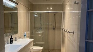 A modern bathroom with a glass-enclosed shower, a white sink, and a beige tiled floor. - Avon Homestay (Northam)