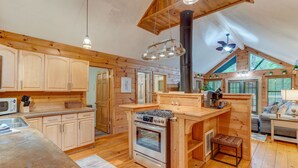 A spacious kitchen with wooden cabinets, a central island with a stove, and a large window. - Bamby Bungalow. Family and Pet Getaway. Fenced in yard and minimal stairs (Ellijay)