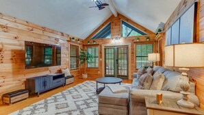 A log cabin interior with a sofa, ottoman, TV, and a ceiling fan. - Bamby Bungalow. Family and Pet Getaway. Fenced in yard and minimal stairs (Ellijay)