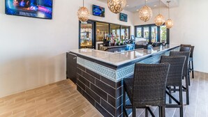A bar area with a counter, bar stools, hanging pendant lights, and a television screen displaying a concert. - 9Br/6Ba lake view Pool House from 330/NT, Close To Disney (Kissimmee)