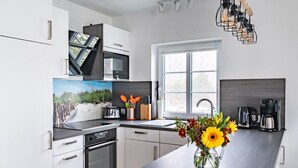 Een moderne keuken met witte kasten, een ingebouwde oven, een groot raam en een vaas met bloemen op het aanrecht.
