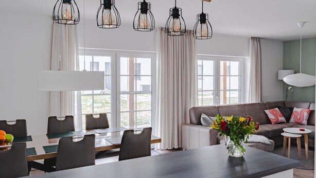 Een moderne keuken met een centraal eiland, een eethoek met stoelen, een bank met kussens en een vaas met bloemen.